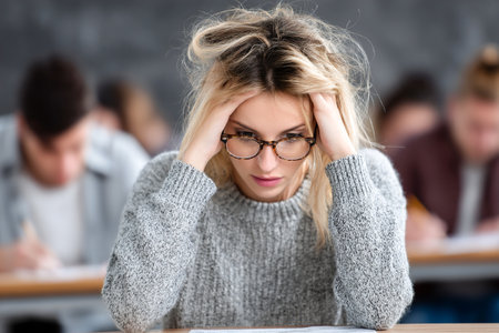 A student displays a worried expression while taking a test, surrounded by classmates in a classroom. The atmosphere is tense as everyone focuses on their work.の素材