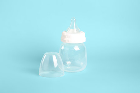 A clear milk bottle sits on a light blue background. The bottle has a white lid placed beside it. The scene shows a simple setup for feeding infants or young children.の写真素材