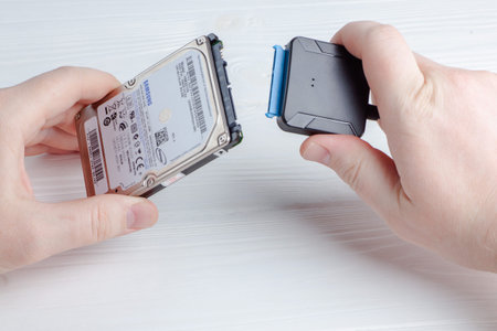 Hands hold a Samsung HDD disk while connecting it to a USB adapter. The setup is for transferring...