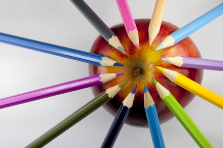 Color pencils forming a circle with their tips on a red and yellow apple against a white background の写真素材