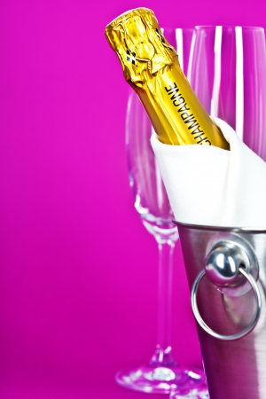 Champagne bottle in cooler and two champagne glasses on pink backgroundの写真素材