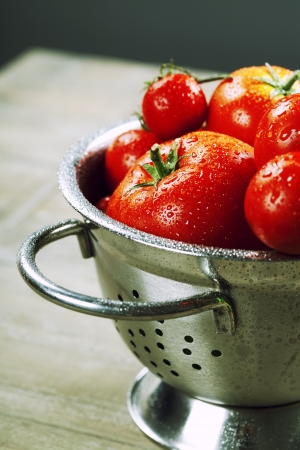 fresh tomatoes  in metal colander  and herbs on a wooden tableの写真素材