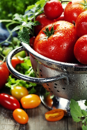 fresh tomatoes (in metal colander) and herbs on a wooden tableの写真素材