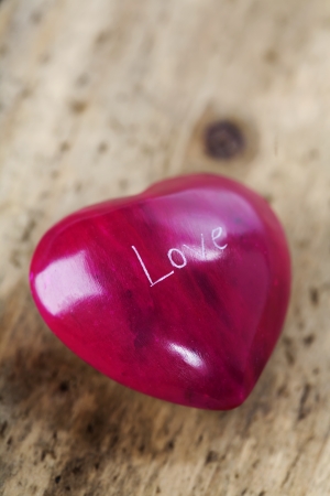 Photo of a heart-shaped red stone on wooden boardの写真素材