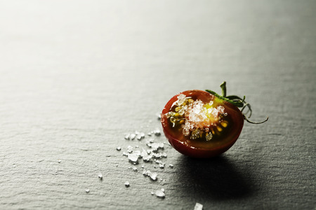 Fresh grape tomatoes with  salt for use as cooking ingredients with a halved tomato in the foreground with copyspaceの写真素材