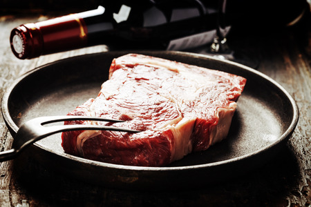 Marbled beef steak in a frying pan with a bottle of wine and wine glass on old wood backgroundの写真素材