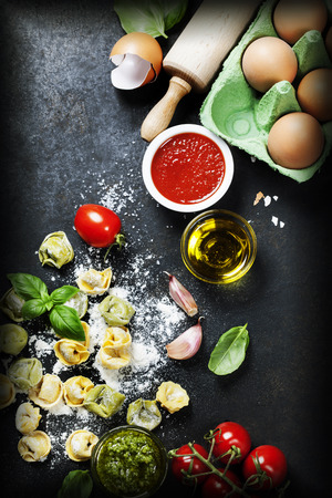Homemade raw Italian tortellini, basil leaves  with flour and  tomatoes on dark vintage backgroundの写真素材