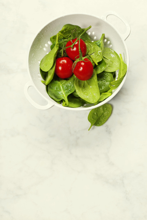 fresh organic garden vegetables in colander bowl on white rustic stone background, healthy cooking conceptの写真素材
