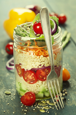 Cucumber, quinoa, tomato, onion, carrot and mint salad in a jar  on rustic wooden tableの写真素材