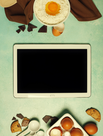 Baking background with ingredients for making chocolate chip cookies and tablet computer on blue rustic table. Top view. Flat lay style. Cooking meets technologyの写真素材