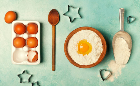 Baking background with flour, eggs and kitchen tools on blue rustic table. Top view. Flat lay style.