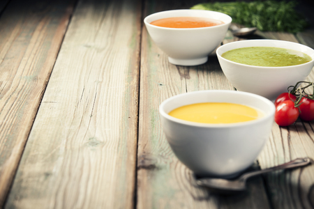 Variety of cream soups - tomato, broccoli and pumpkin soups over wood background. Copy spaceの写真素材