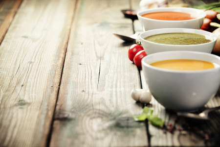 Variety of cream soups - tomato, broccoli and pumpkin soups over wood background. Copy spaceの写真素材