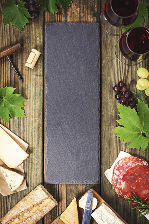 Food frame. Wine and snack set with red wine in glasses, meat variety, bread, cheese and grape on   rustic wooden background, top view, copy space in centerの写真素材