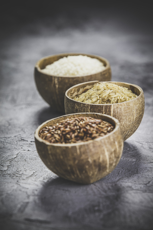 Assortment of different rice in bowls: Rice berry, Brown rice and Risotto rice on grey stone background.の写真素材