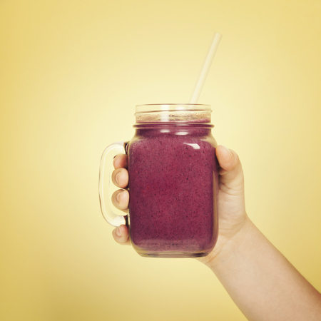 Woman (teenage girl) hand holding smoothie shake against bright wall. Drinking  healthy smoothie conceptの写真素材