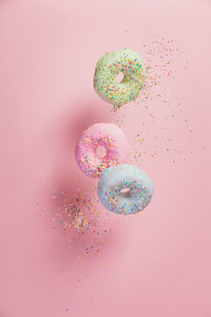 Sweet and colourful doughnuts with sprinkles falling or flying in motion against pastel pink backgroundの写真素材