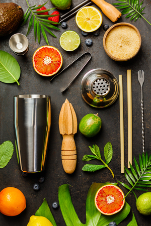 Cocktail making bar tools, shaker, tropical fruits and leaves on a dark background. Top viewの写真素材