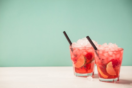 Red drink with ice. Cocktail making bar tools, raspberry, lime, oranges and mint leaves. Raspberry mojito on blue backgroundの写真素材