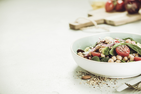 Healthy vegan energy boosting salad with chickpeas, broccoli, tomatoes, red onion, spinach and nuts in blue plate on concrete background, selective focus. Clean eating, superfood, vegan, detox food conceptの写真素材