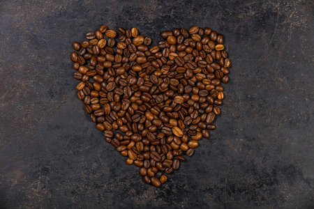 Coffee beans in shape of heart on dark rustic background