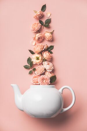 Creative layout made of whte tea pot with orange roses on pink background, flat layの写真素材