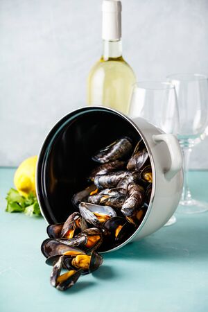 Pot of steamed mussels with lemon, herbs and white wine on blue backgroundの写真素材