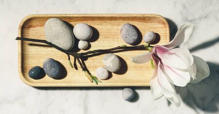 Flat lay composition with beautiful spring magnolia flowers and grey stones on white marble background. Relaxation and zen like concept.の写真素材