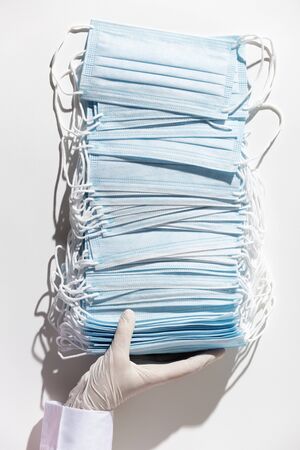 Doctor hands in latex gloves holding a stack of facial medical masks, white background, close upの写真素材