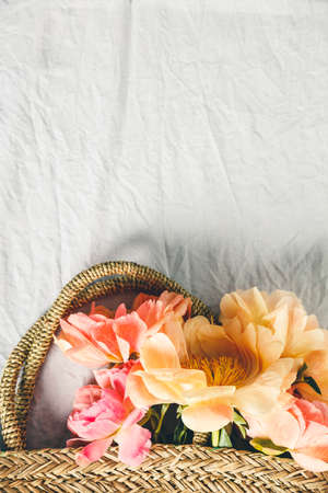 Flat-lay of Beautiful peony flowers in straw bag over grey linen table cloth backgroundの写真素材