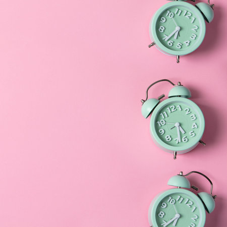 Creative layout of green alarm clocks on pastel pink background. Minimal concept.
