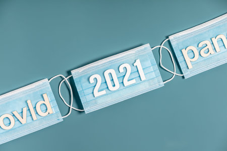Surgical masks with number 2021 and words covid and pandemic on blue