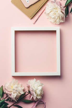 Creative flat lay with flowers, notebook, glasses, mobile phone and white wooden frame on pink backgroundの写真素材