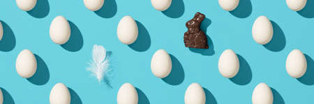 Pattern made of white eggs, chocolate banny and bird feather on blue background, bannerの写真素材