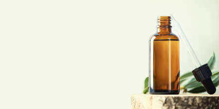 Banner with Blank transparent amber glass essential oil bottle and pipette on wooden slice podium, Beauty blog, salon treatment concept, minimalism brand packaging mock up, copy spaceの写真素材