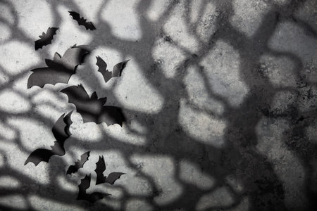halloween and decoration concept - black paper bats, moonlight and scary trees shadows background