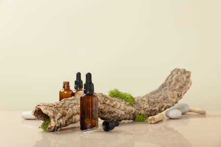 Trendy composition of Blank amber glass essential oil bottles, dried branch and moss on beige background. Product, cosmetic, perfume, jewellery mock upの写真素材