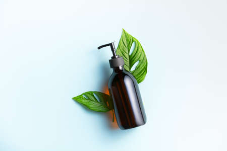 Banner. One cosmetic dark amber glass bottle with green plant on blue backgroundの写真素材