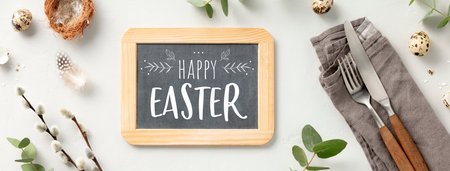 Easter composition, table setting with chalkboard, white plate, golden cutlery, easter eggs and spring branches on light grey background top view flat layの写真素材