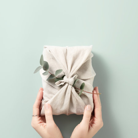 Female hands holding a gift in eco friendly reusable fabric package on blue backgroundの写真素材