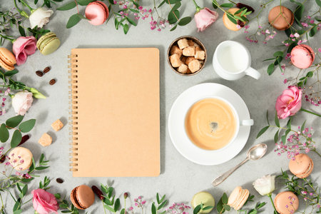 White cup of coffee, empty notebook and Frame made of Spring flowers and different types of macaroons flat lay mock up copy spaceの写真素材