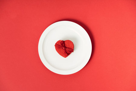 Valentines day concept. White plate with heart shaped gift box on red backgroundの写真素材