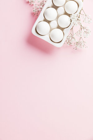 White eggs in white ceramic holder and flowers on pink backgroundの写真素材