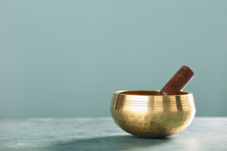 Golden Tibetan singing bowl with a wooden mallet placed on a table, symbolizing peace and mindfulness in meditation practice.の写真素材