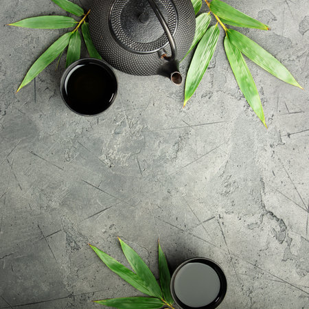 Flat lay of a traditional black teapot, tea cups, and green leaves on a textured dark stone surface with copy space â perfect for menus, spa, or tea branding.の写真素材
