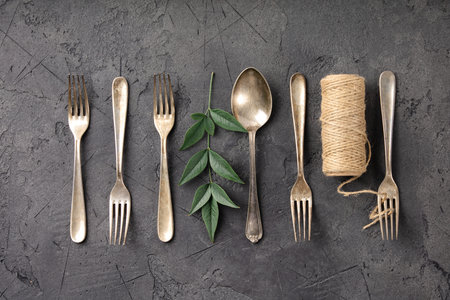 A cohesive collection of rustic kitchen flat-lay compositions featuring vintage silverware, assorted spices, herbs, coarse salt, peppercorns, nuts, dried chili, star anise, wooden utensils, ceramic tableware, greenery, fern leaves, and natural twine. The series showcases antique forks, spoons, knives, and ladles arranged on a dark textured stone background in creative patterns and styled culinary scenes. From minimal utensil lineups to botanical and handcrafted accents, this versatile collection is ideal for culinary branding, food styling, recipe blogs, restaurant graphics, menu layouts, and traditional cooking themes.の写真素材