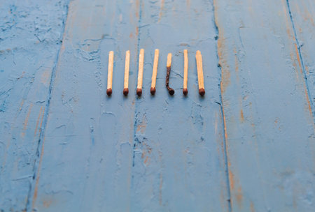 Seven wooden matches on a blue table, one match burned