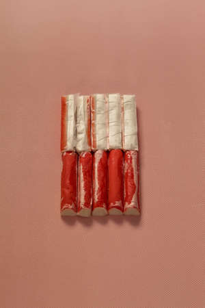 The vertical image shows frozen crab sticks. They lie close to each other. There are ten of them. They're medium-sized. Each piece is packed in a separate transparent packageの写真素材