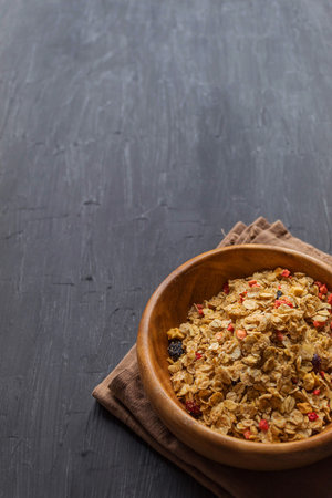 Muesli with raisins, dried cranberries and strawberries in a wooden plate on a black background