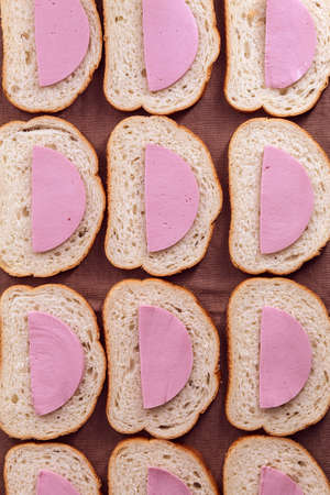 Sandwiches of white bread and boiled sausage lie on a kitchen towelの写真素材